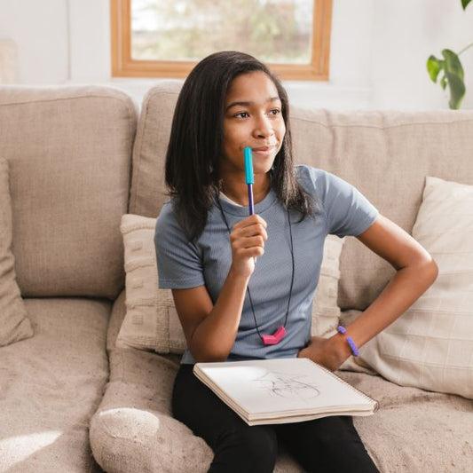 Flicka sitter i soffa och tuggar på penna med Krypto-Bite tuggtopp för ökat fokus.