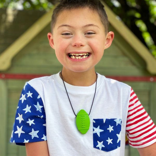 Leende pojke med limegrönt tugghalsband i form av rugbyboll runt halsen