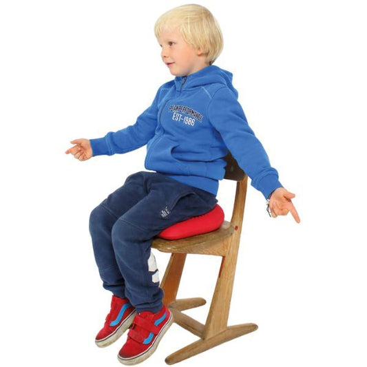 Barn balanserar på en röd Dynair Wedge sittkudde på en trästol med utsträckta armar