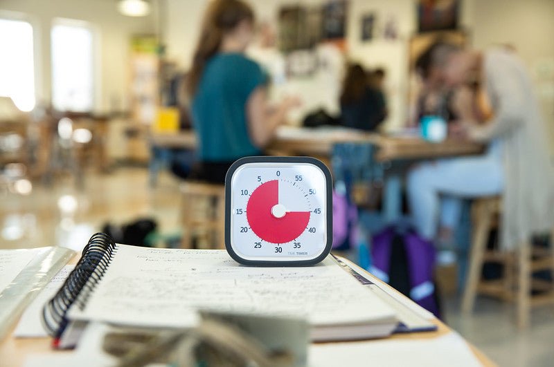 Time Timer MOD placerad på ett skrivbord i ett klassrum, omgiven av anteckningar och skolmaterial.