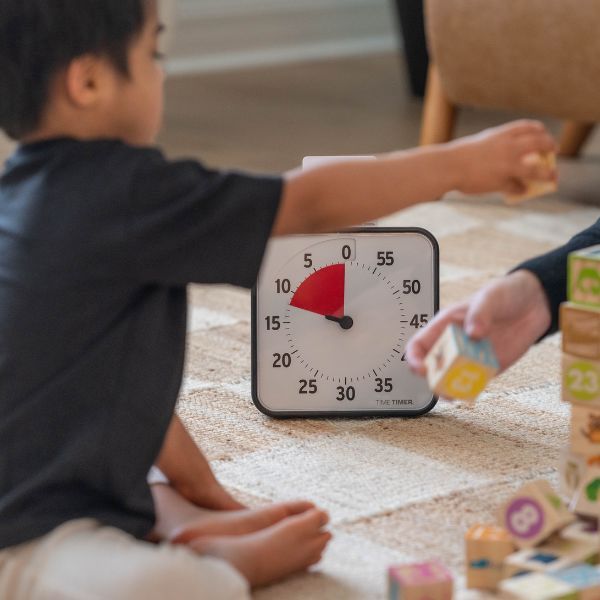 Barn bygger med klossar med tidshjälpmedel Time Timer i bakgrunden.