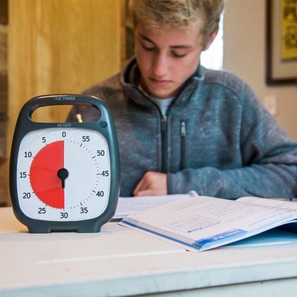Tonåring gör läxor med Time Timer Plus på skrivbordet framför sig.