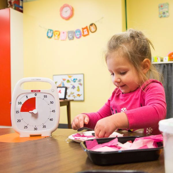 Flicka pysslar med Time Timer Plus bredvid sig på bordet i förskolemiljö.