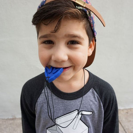 Barn biter på ett blått tugghalsband Dino-Tracks och ler mot kameran