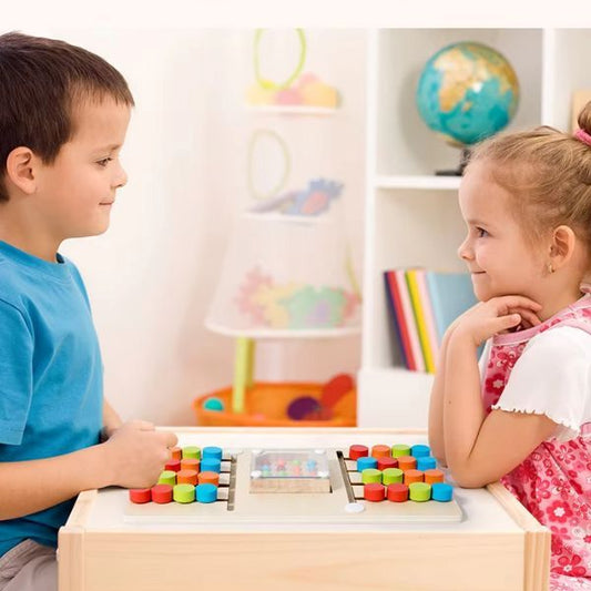 Två barn sitter mittemot varandra och spelar Färgkampen på ett bord i en färgglad och trygg miljö.