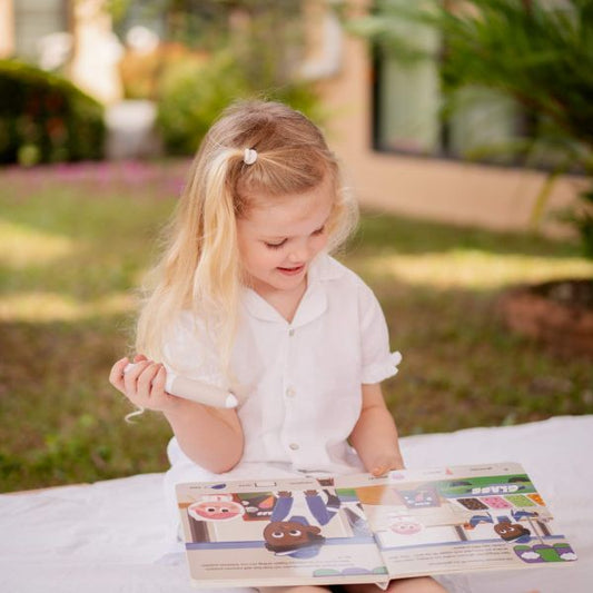Flicka sitter ute och läser boken Vem går vilse med Readioo-läspenna.