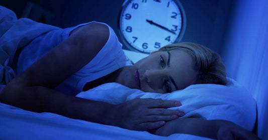 Kvinna ligger vaken i sängen med en klocka i bakgrunden som visar sen natt, symboliserar sömnproblem vid ADHD.