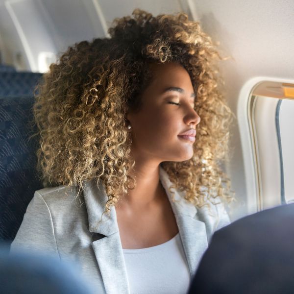  Person med slutna ögon slappnar av i flygplansstol tack vare hörselskydd.