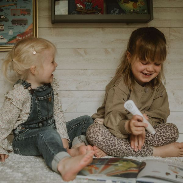 Två barn sitter på golvet och skrattar medan de använder Readioo läspenna med boken Bokstäver.