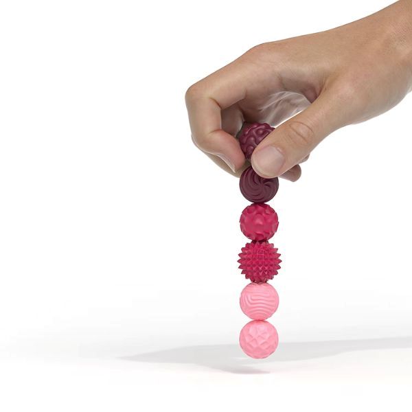 Hand som håller magnetiska sensoriska fidgetbollar i rött och rosa – visuellt hjälpmedel för fokus och stresslindring