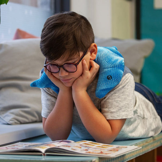 Barn läser med Manimo Tyngddelfin över axlarna, sensoriskt tyngddjur för lugn och fokus vid NPF.