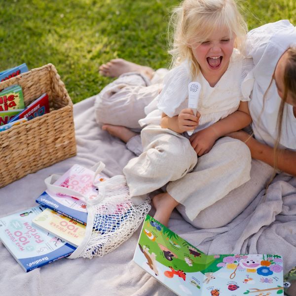 Flicka med Readioo läspenna och boken "Mina första 100 ord: Djur" under picknick utomhus.