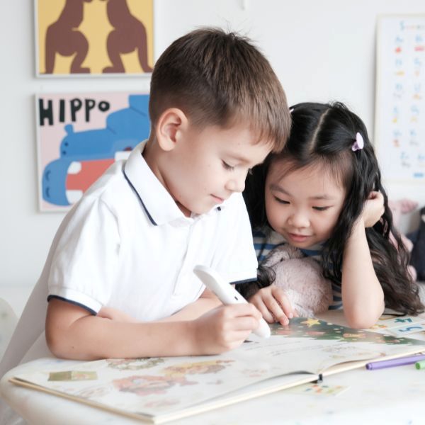 Två barn använder Readioo läspenna vid bordet med en bilderbok.
