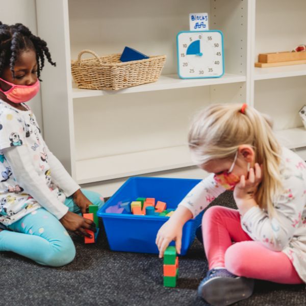 Två barn leker och bygger med klossar i klassrumsmiljö, med en blå Time Timer Medium i bakgrunden.