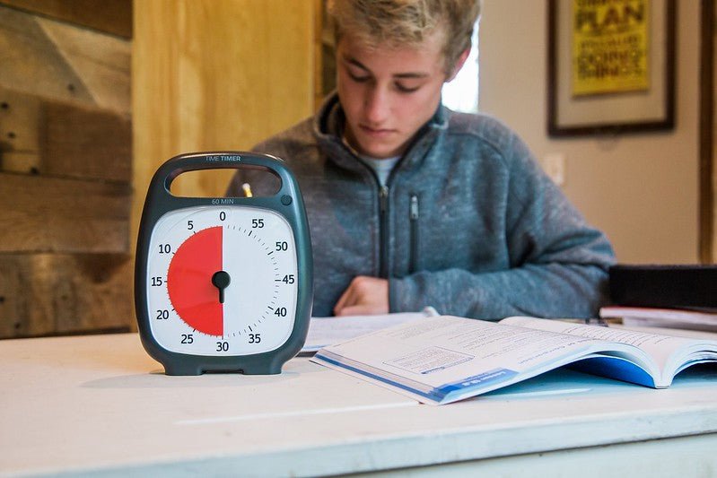 Time Timer Plus i svart används av en student som studerar vid ett skrivbord, vilket visar dess användning i inlärningsmiljöer.