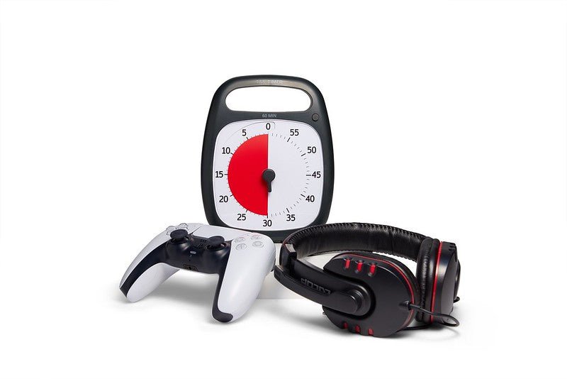 Time Timer Plus i svart bredvid ett par hörlurar och en spelkontroll, ett verktyg för att skapa tidshantering och fokus i spel eller aktiviteter.